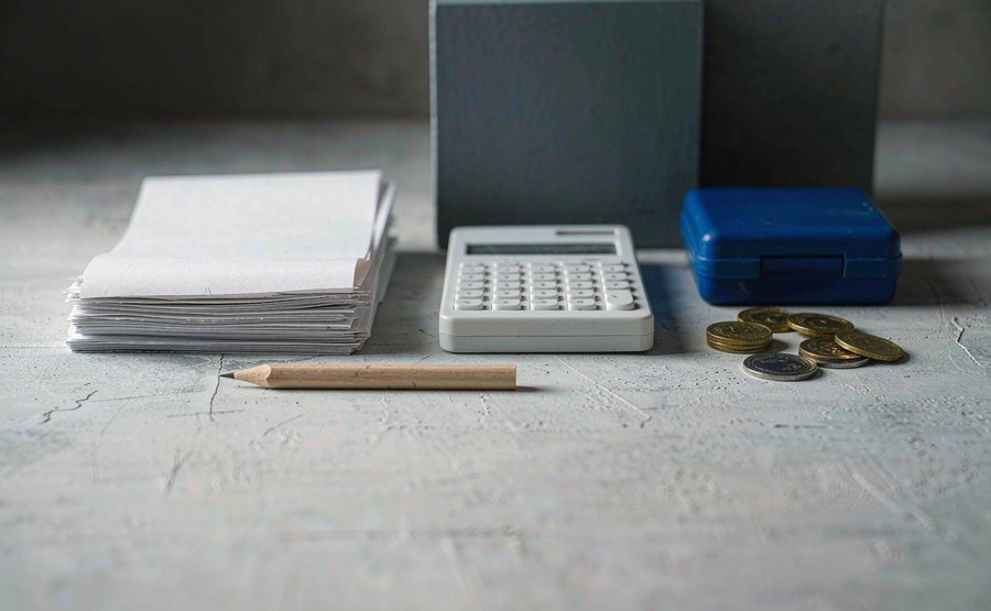 A stack of paper receipts, a pocket calculator, a pencil and loose coins on a light grey desk
