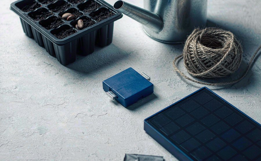 A seed tray of potting soil, dried seeds, garden twine, a watering can spout and a small solar panel on a desk