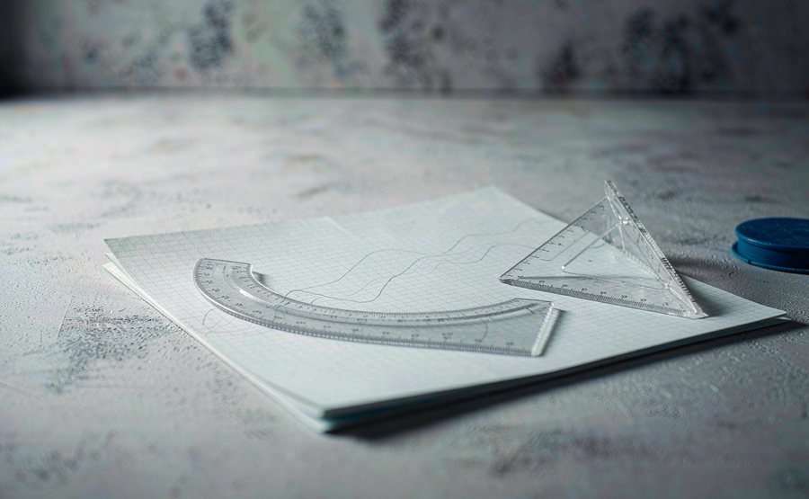 A sheet of graph paper with faint pencil curves, a french curve ruler and a set square on a grey desk