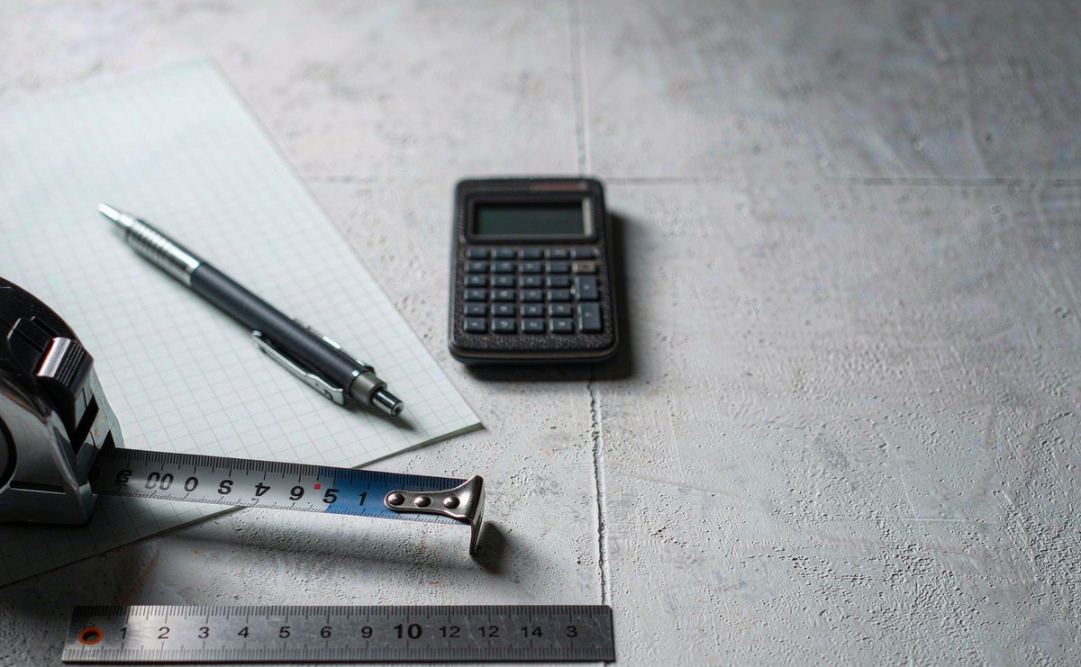 A tape measure, pocket calculator, steel ruler and sheet of graph paper laid out on a light grey desk